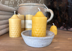 Beeswax candles with textured surface in a concrete holder on a wooden surface.