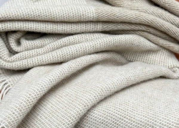 A double weight Relish wool blanket in gray and beige colors with a herringbone pattern and cobb weave border, displayed on a wooden rod.