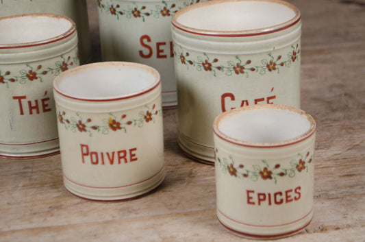 Set of five vintage French ceramic kitchen canisters with hand-painted floral decoration and red lettering displayed on a wooden table.
