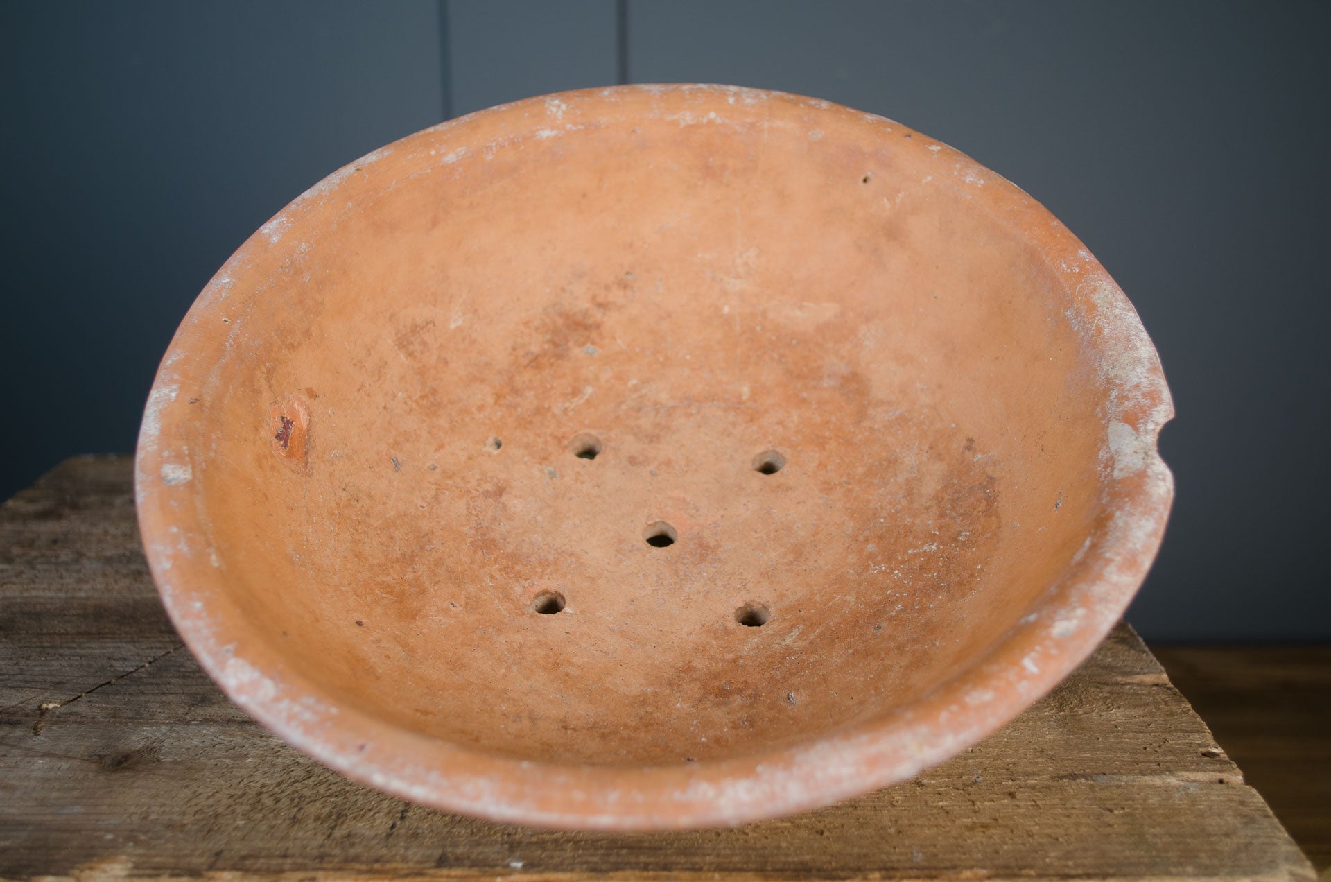 Terracotta pot with holes on a wooden surface against a dark background