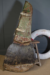 Vintage wood rudder on a stand with a life preserver in the background.