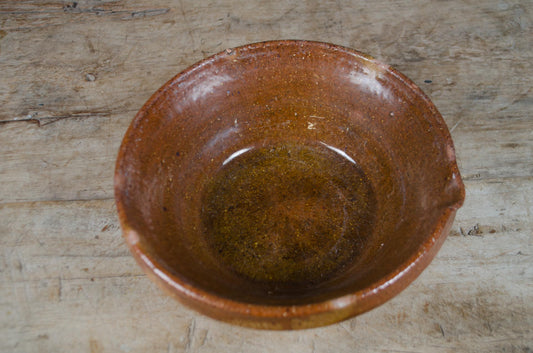 Antique French glazed terracotta dairy bowl with pouring lip and rich brown glaze on a rustic wooden table.
