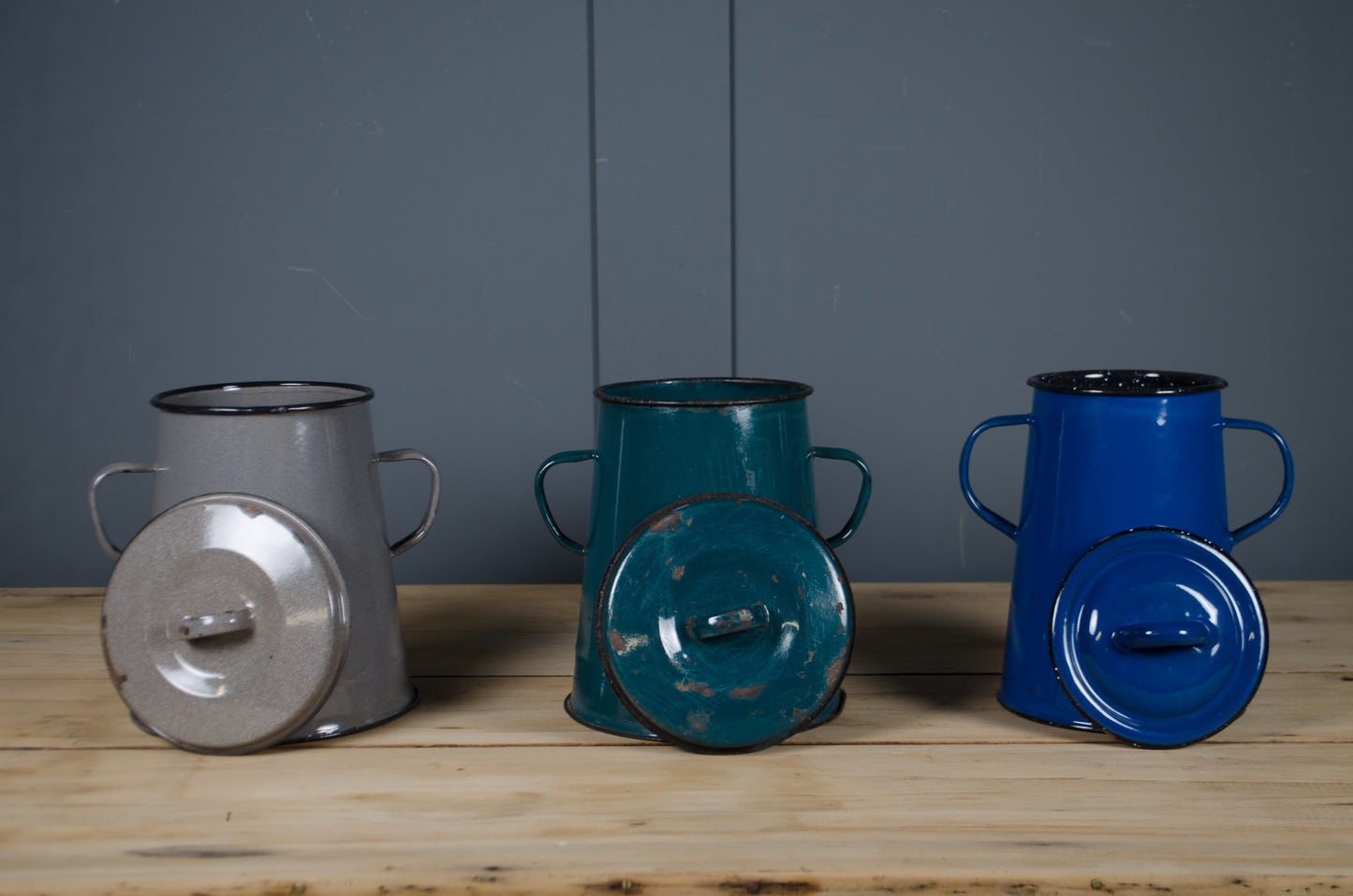 enamel canisters for food compost waste grey, teal, and blue on a wooden surface with a dark grey background.