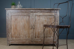 Vintage wooden cabinet with a rustic metal chair against a dark blue wall.