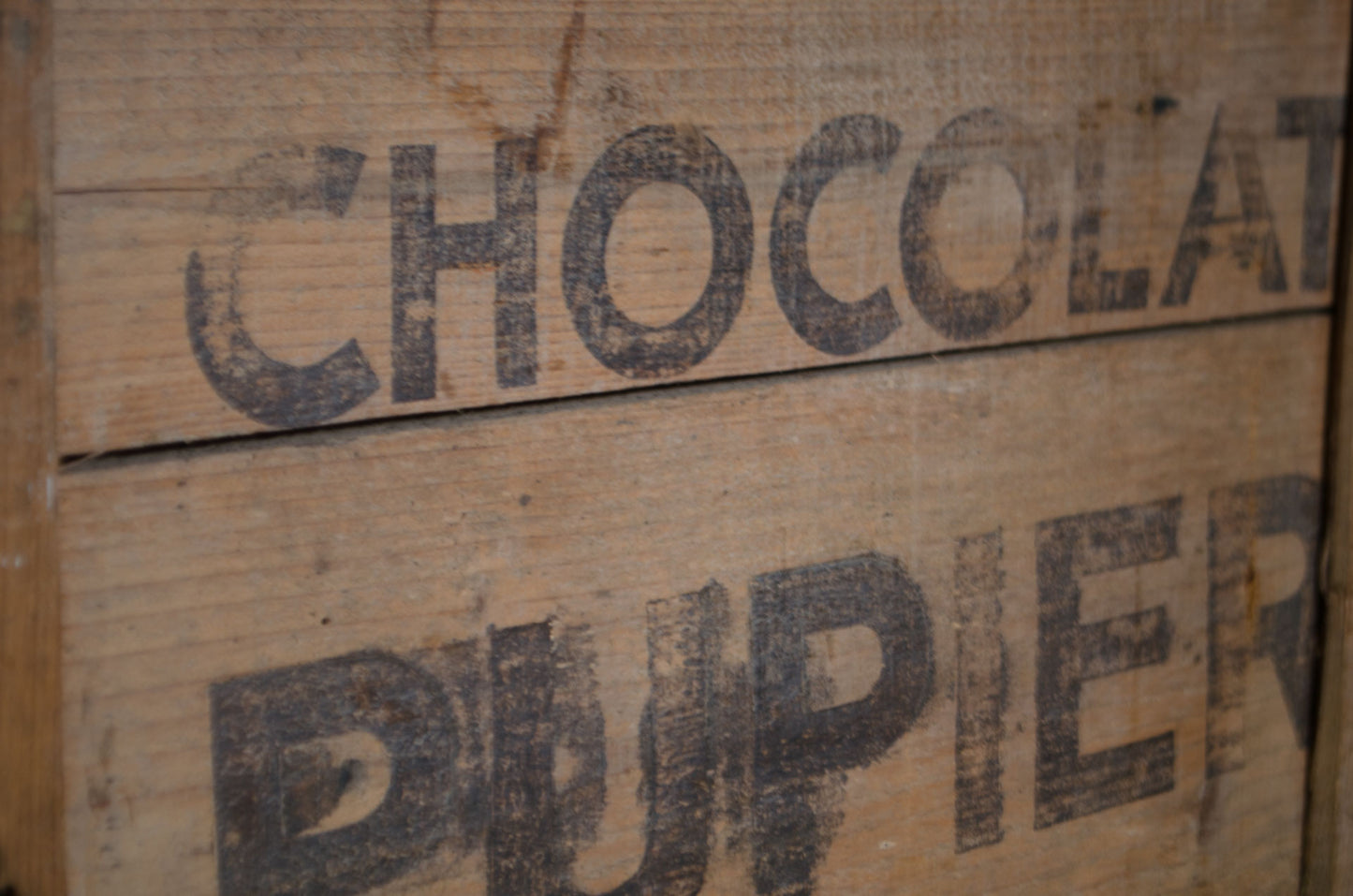 Close-up of a rustic wooden box or crate with the words 'CHOCOLAT DU PIER' printed in dark stencil-style lettering on the front.