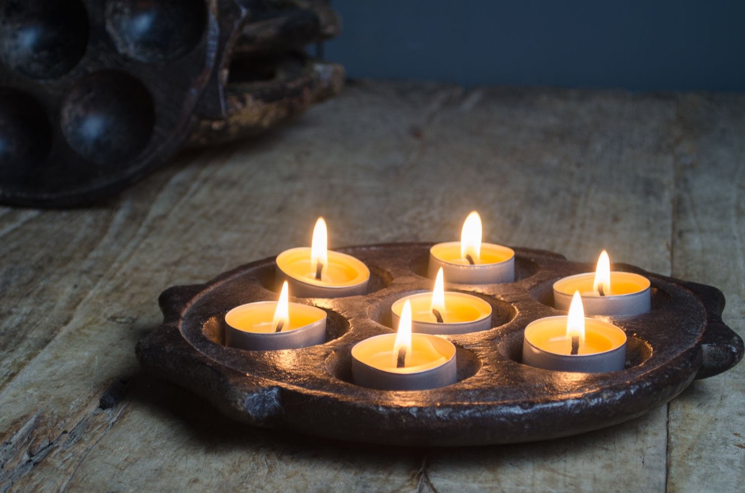 A hand carved stone Indian tealight holder with multiple lit tealight candles placed on a wooden surface.