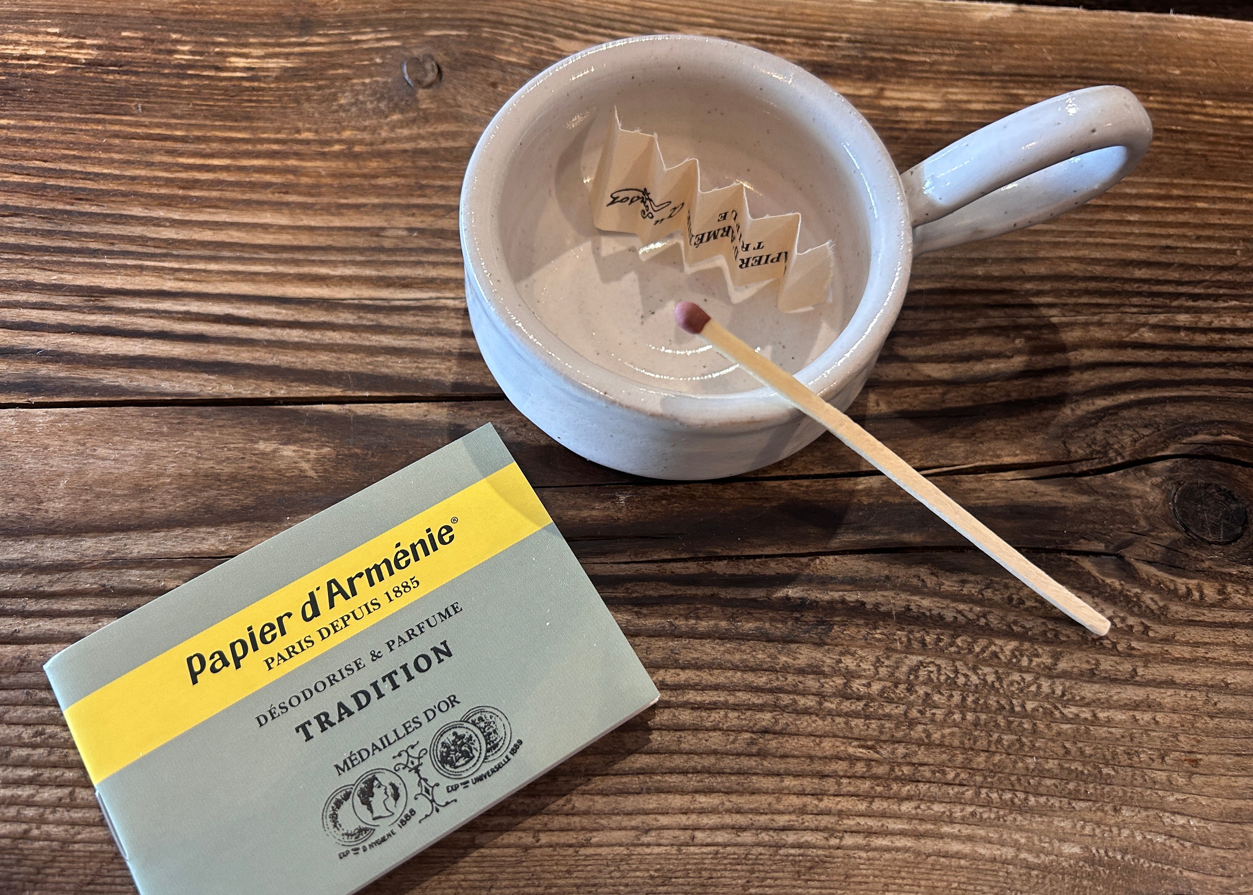 Papier d'Armenie paper burning with a matchbox and a cup on a wooden surface.  Armenian paper insence natural fragrance for your home