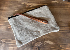 Grey clutch bag with a brown strap on a wooden surface