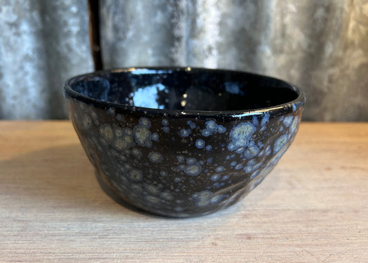 Blue hand thrown ceramic bowl with blue speckles on a bleached wood table