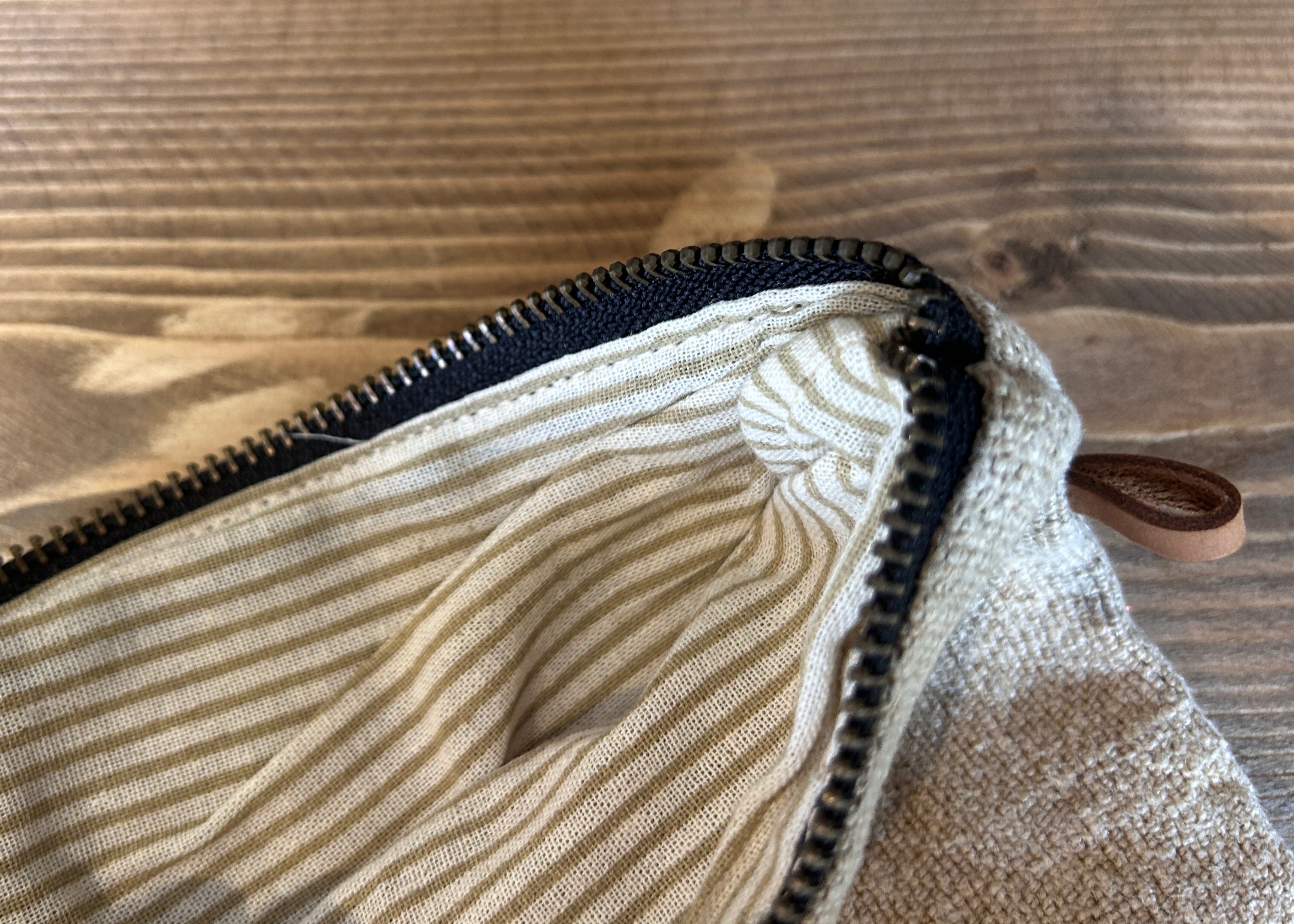 Close-up of a beige fabric pouch with a zipper on a wooden surface