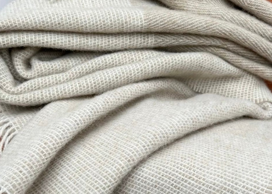 
A double weight Relish wool blanket in gray and beige colors with a herringbone pattern and cobb weave border, displayed on a wooden rod.