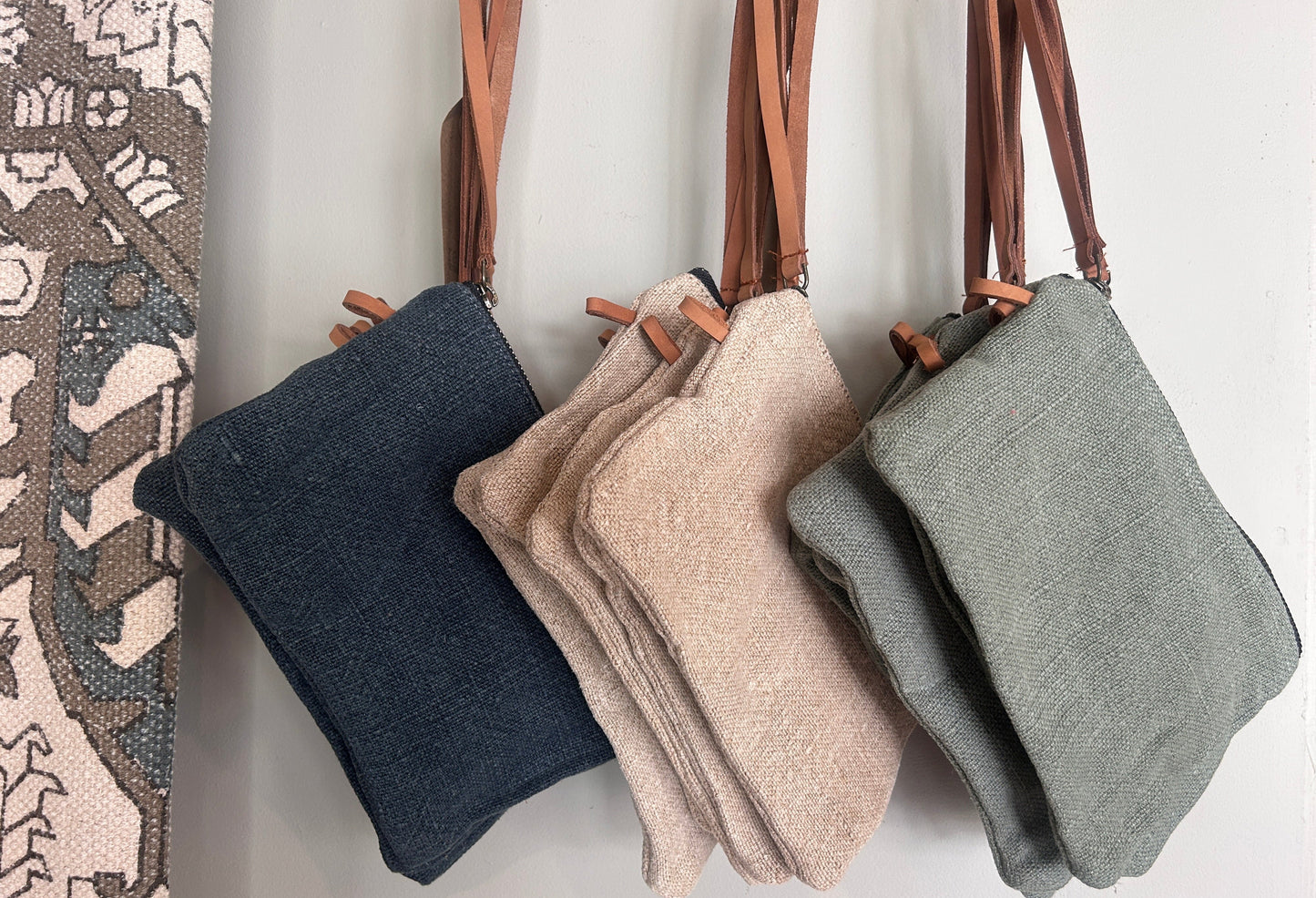 Three handbags in navy, beige, and gray hanging on a rack against a neutral background.