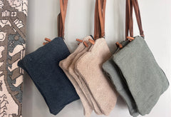 Three handbags in navy, beige, and gray hanging on a rack against a neutral background.