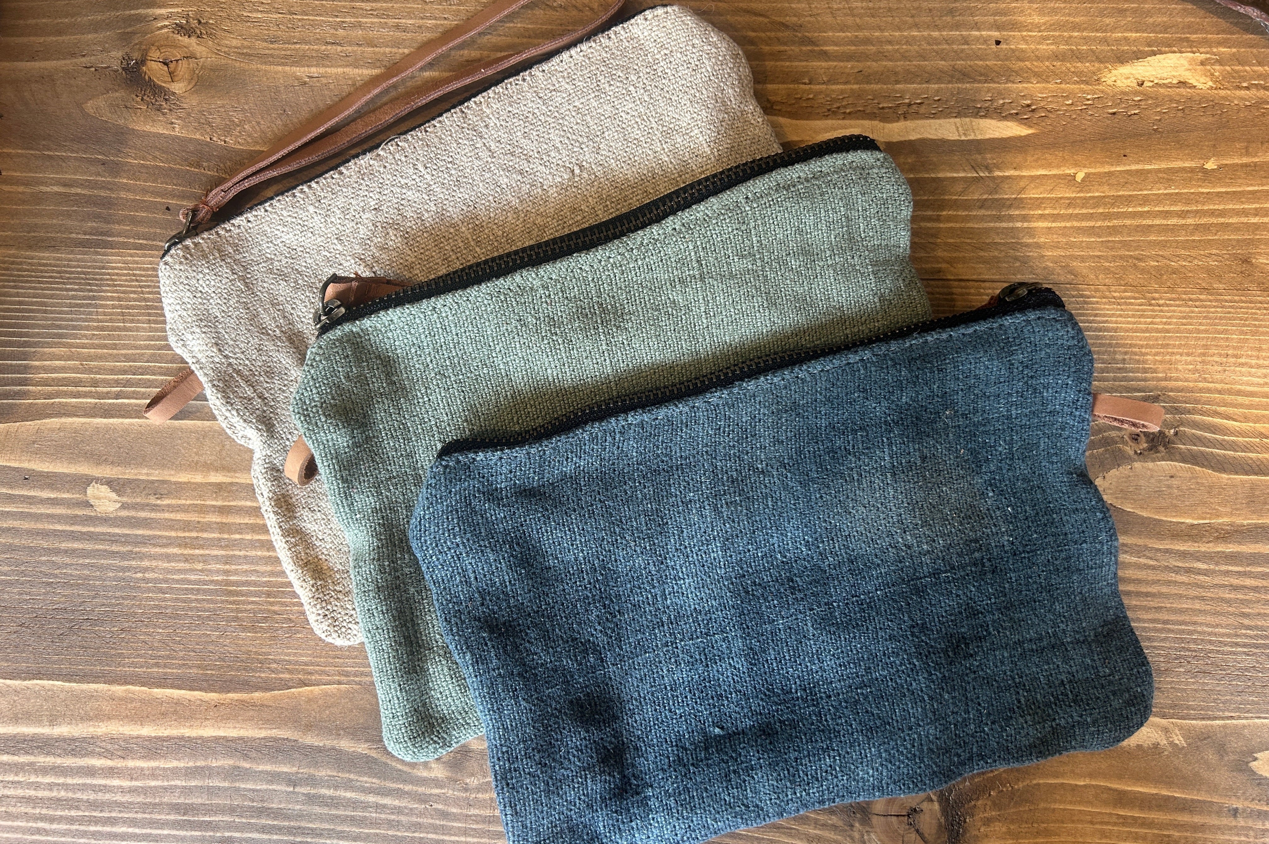 Three fabric pouches in beige, green, and blue on a wooden surface