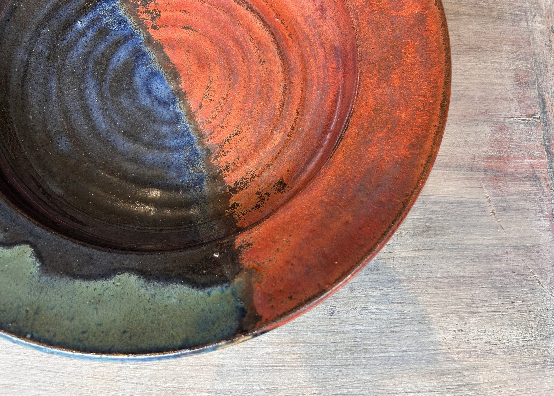
Close-up of a ceramic plate with concentric circular patterns in red, blue, and black on a wooden surface.