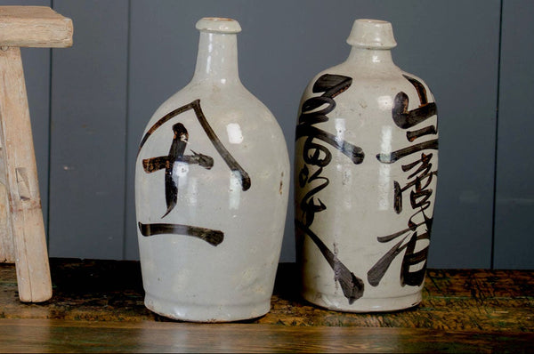 Three ceramic bottles with black characters on a wooden stool against a gray wall.