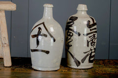 Three ceramic bottles with black characters on a wooden stool against a gray wall.