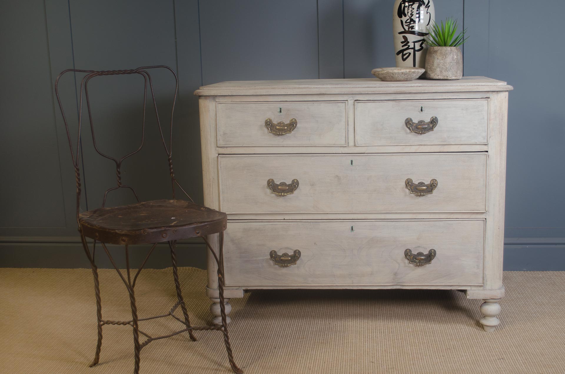 Edwardian pine chest of drawers with bleached finish, antique brass handles, and turned feet against a dark wall background