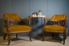 Two yellow velvet antique chairs with wooden frames in front of a blue wall.