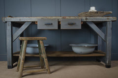 Vintage-style workbench with drawers and a stool against a blue wall.