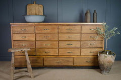 Wooden dresser with multiple drawers, a plant, and a stool against a blue wall.