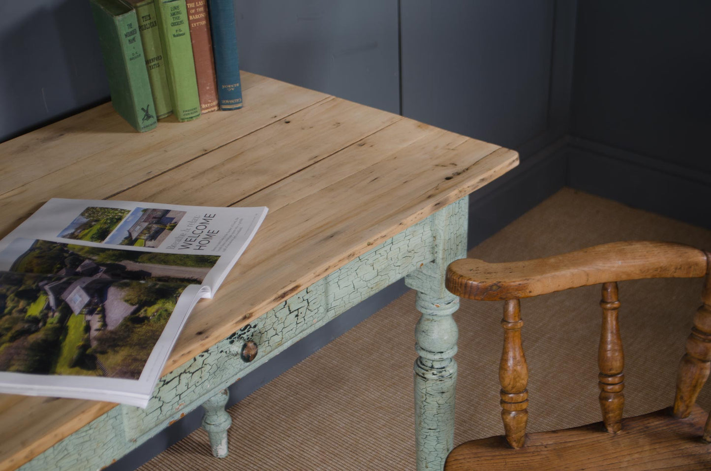 Wooden table with a book on it next to a wooden chair against a dark wall.