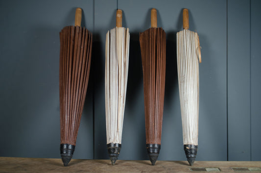 Two pairs of wooden-handled umbrellas against a dark gray wall.