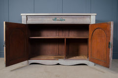 Wooden sideboard with open doors against a blue paneled wall.