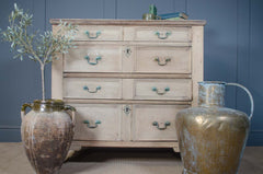 Wooden dresser with distressed finish and teal handles, flanked by two large decorative vases against a blue wall.