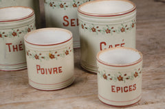 Set of five vintage French ceramic kitchen canisters with hand-painted floral decoration and red lettering displayed on a wooden table.