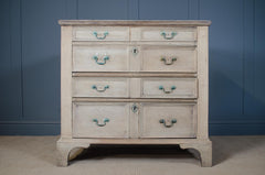 Wooden dresser with distressed finish bleached oak and brass verdigris  handles against a grey wall and sisal carpet