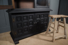 Black wooden cabinet with decorative panels next to a wooden stool on a beige carpet.