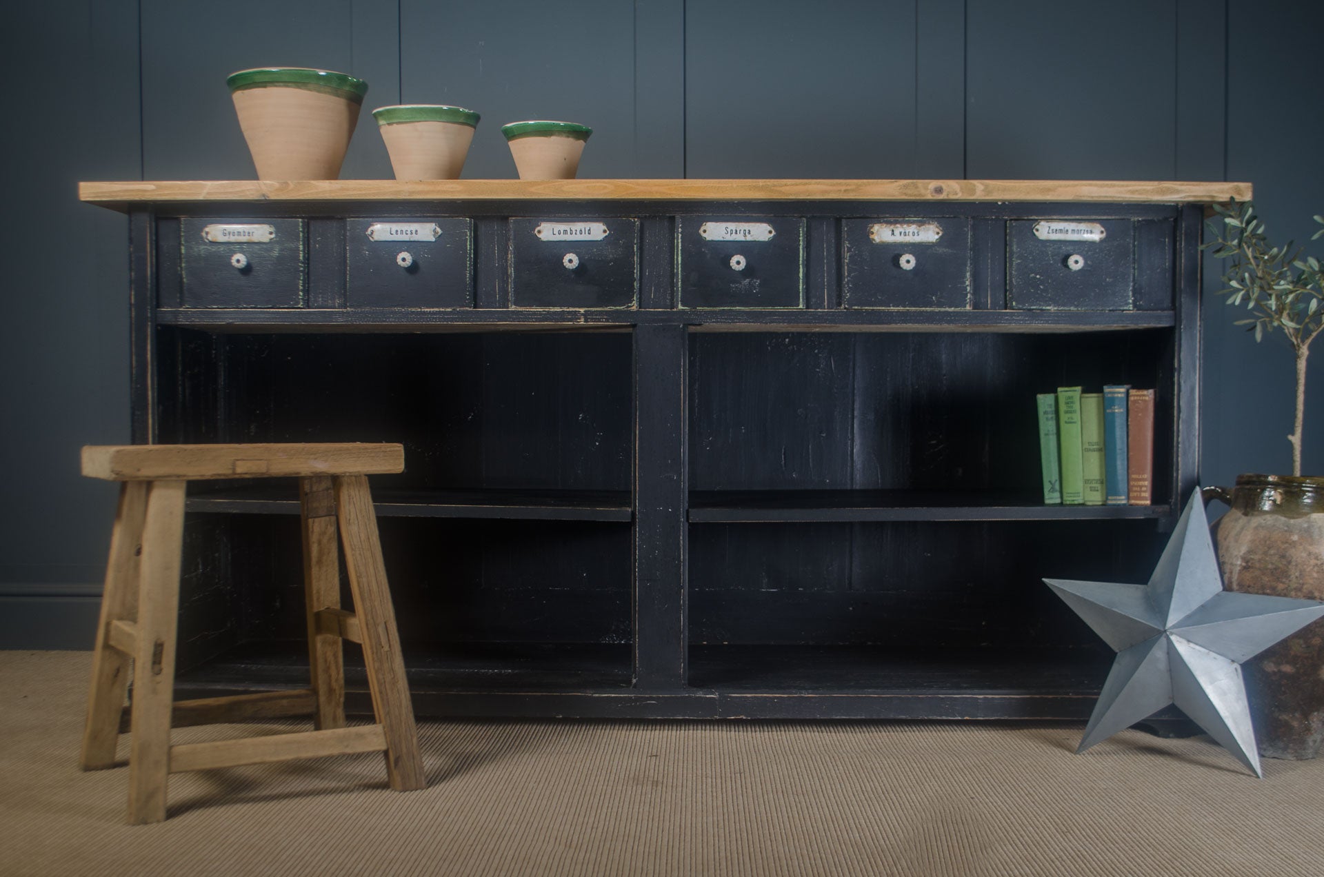 Black metal storage unit with wooden stool and decorative star in a room with dark walls.