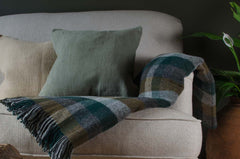Beige sofa with a plaid blanket, cushions, and a mug on a wooden table in a cozy room.