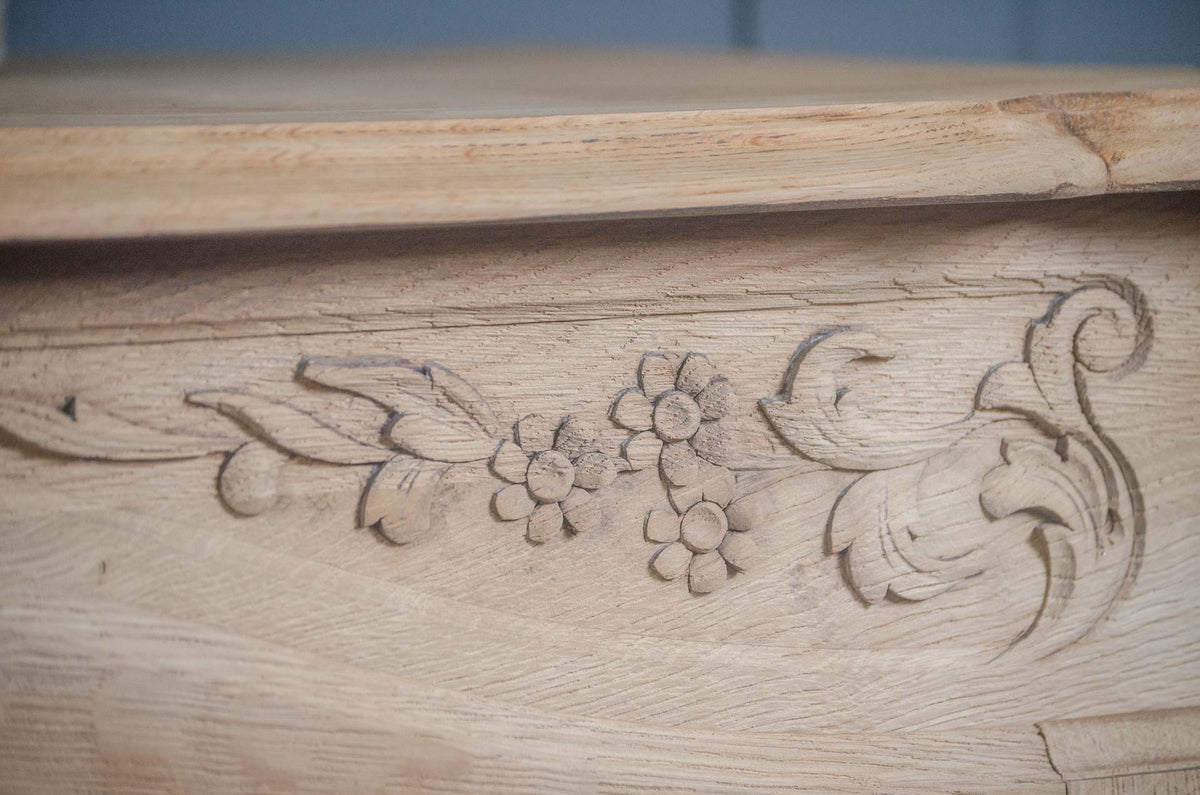
Close-up of a light natural wood oak sideboard surface with carved floral and scroll motifs, showing wood grain and texture.