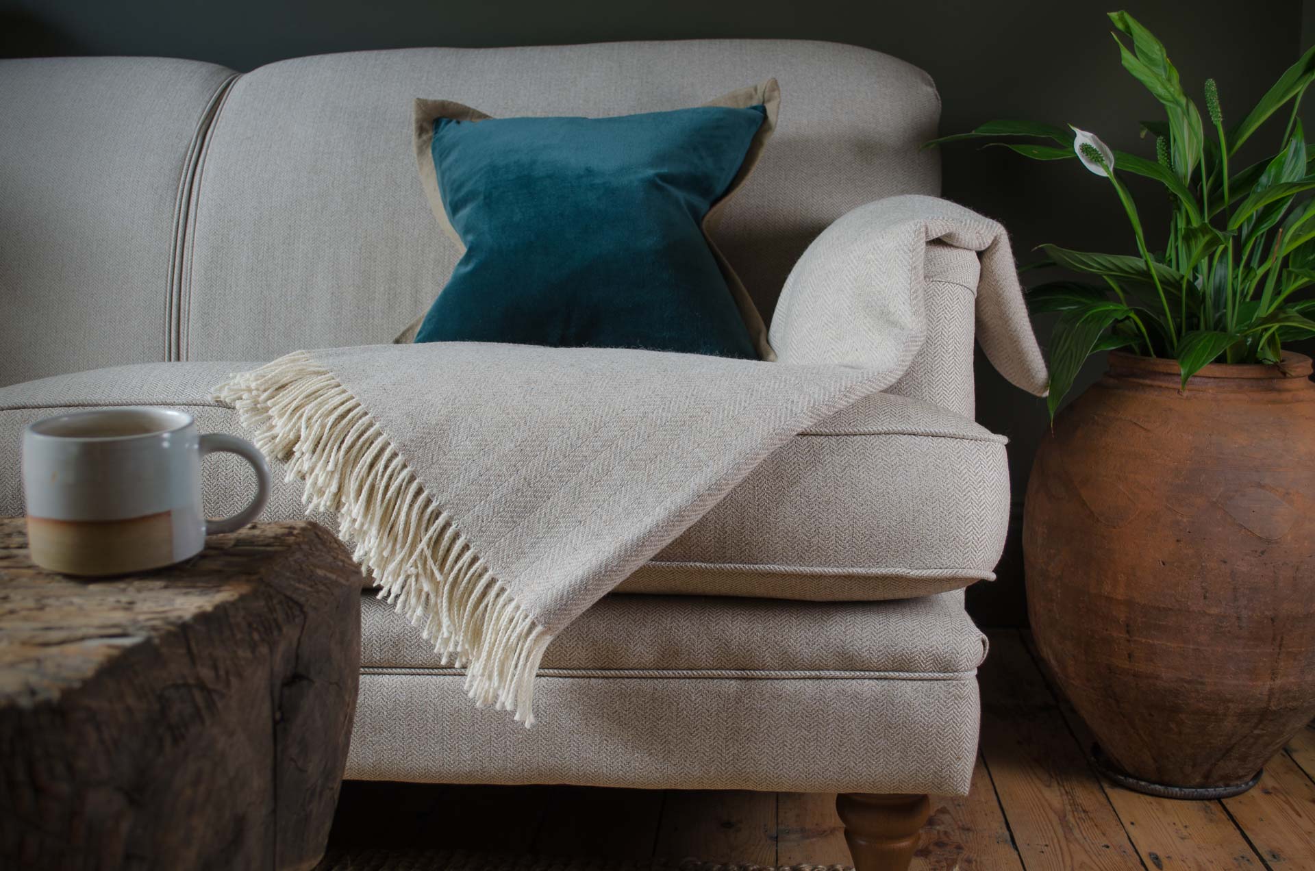 Beige sofa with a blue pillow and white blanket, wooden coffee table with mug, and potted plant on wooden floor. Cotton velvet linen cushion in green