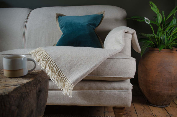 Beige sofa with a blue pillow and white blanket, wooden coffee table with mug, and potted plant on wooden floor. Cotton velvet linen cushion in green
