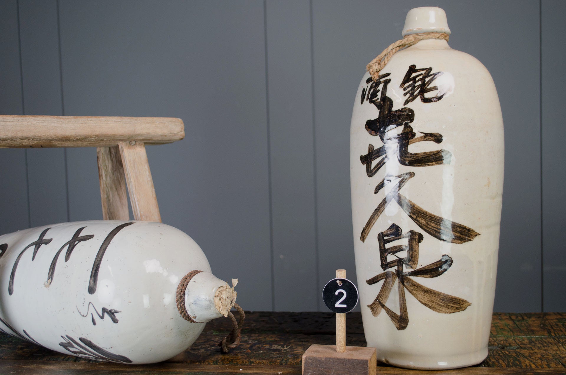 japaense sake bottle made from ceramic with black and beige writing with a grey painted farrow and ball wall and reclaimed kitchen table