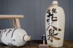 japaense sake bottle made from ceramic with black and beige writing with a grey painted farrow and ball wall and reclaimed kitchen table