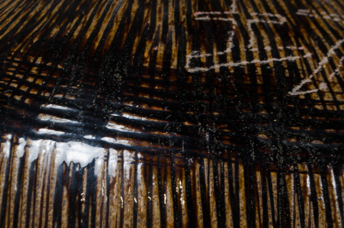 Close-up of a dark brown and black textured surface with vertical striations, a glossy reflective area, and faint white markings in the upper right.