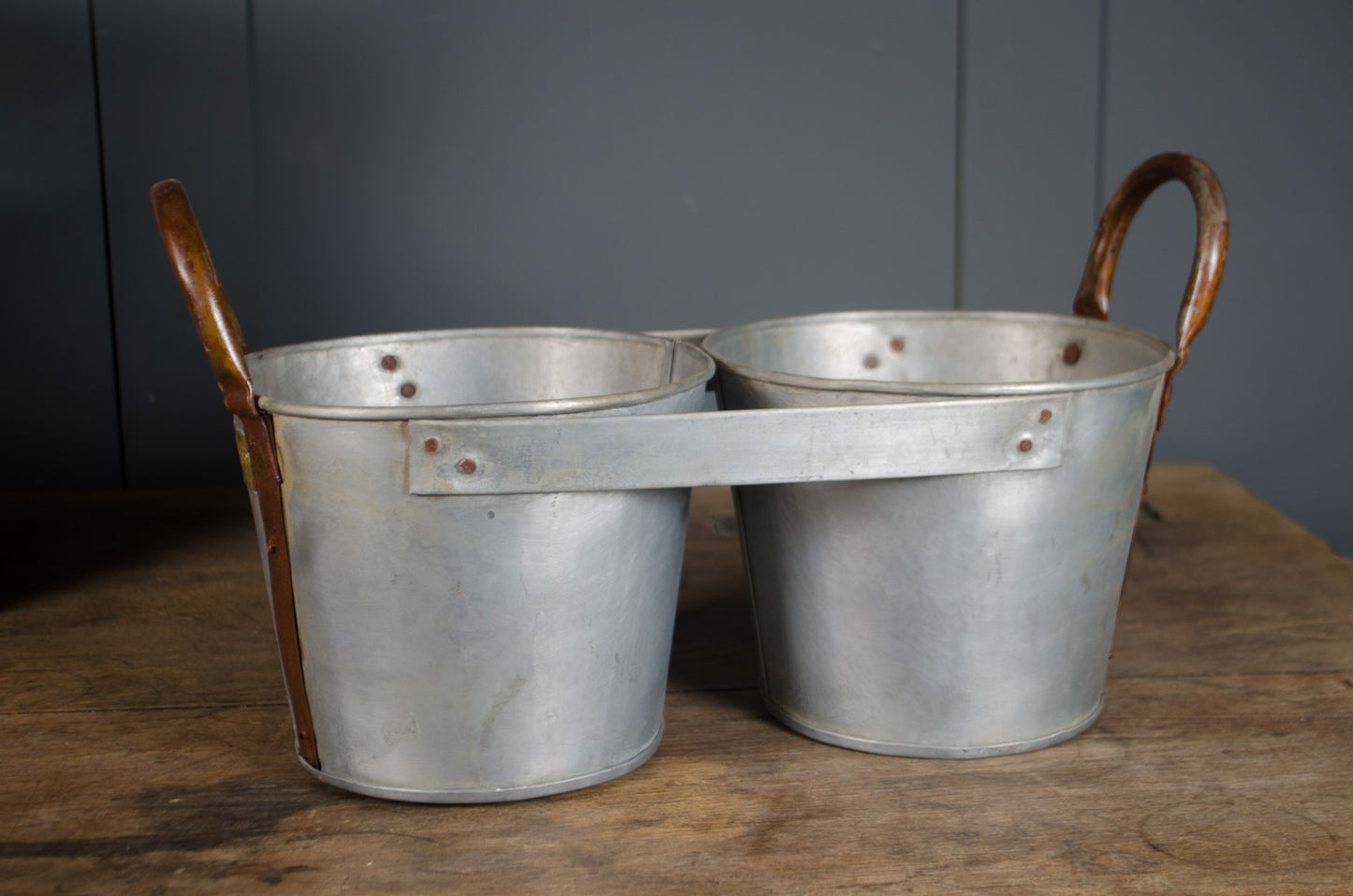 Millwards Two metal buckets with wooden handles on a wooden surface against a gray wall.