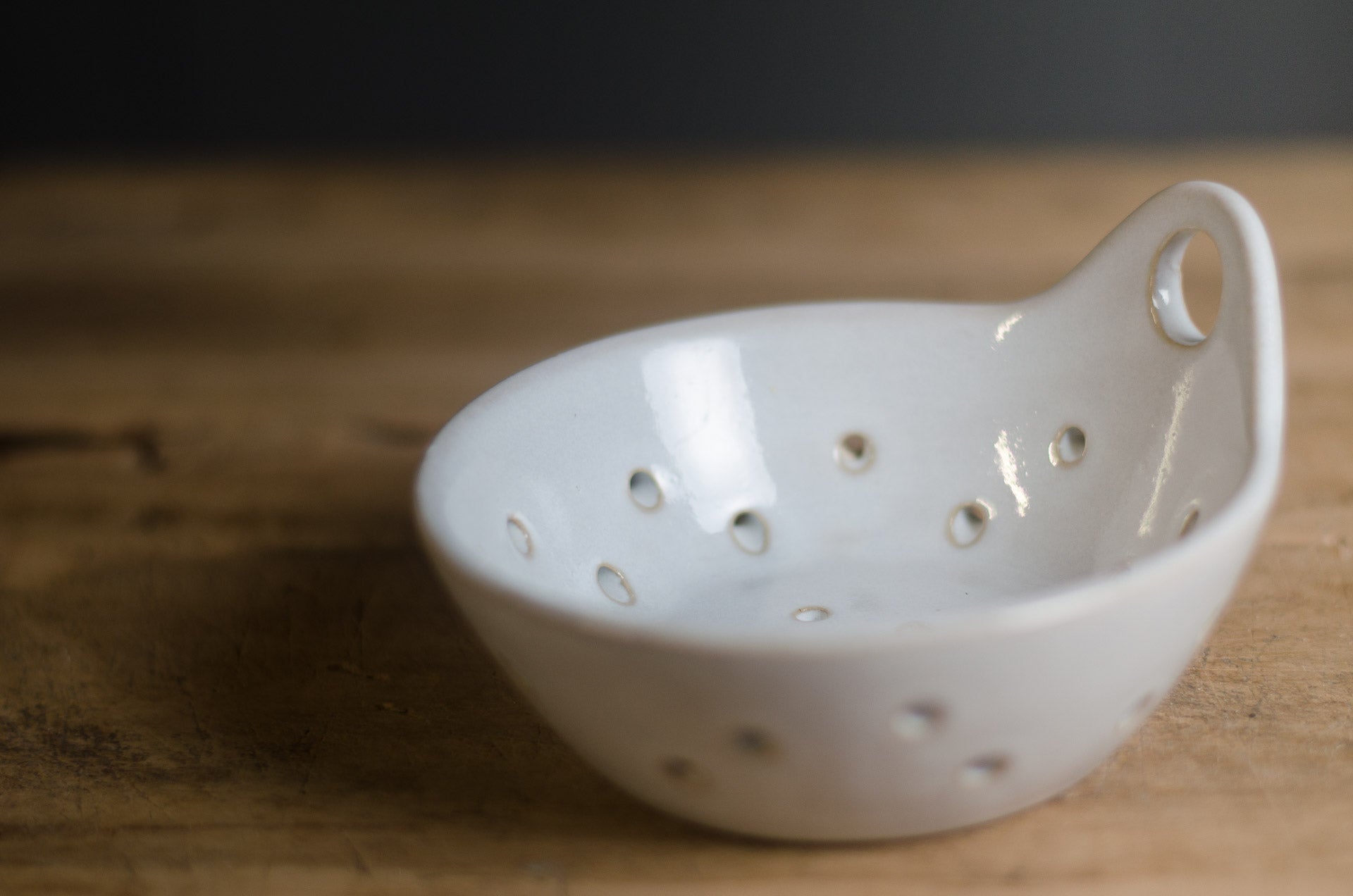 White ceramic berry bowl colander with holes on a wooden surface