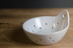 White ceramic berry bowl colander with holes on a wooden surface