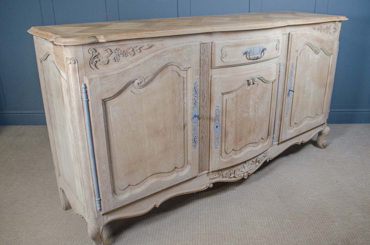 A vintage French-style wooden sideboard cabinet with a distressed cream finish and light blue painted accents, set against a blue paneled wall and beige carpet.