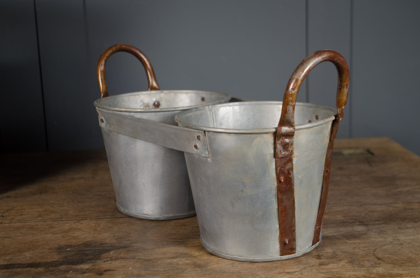 Millwards Two metal buckets with handles on a wooden surface against a gray wall.