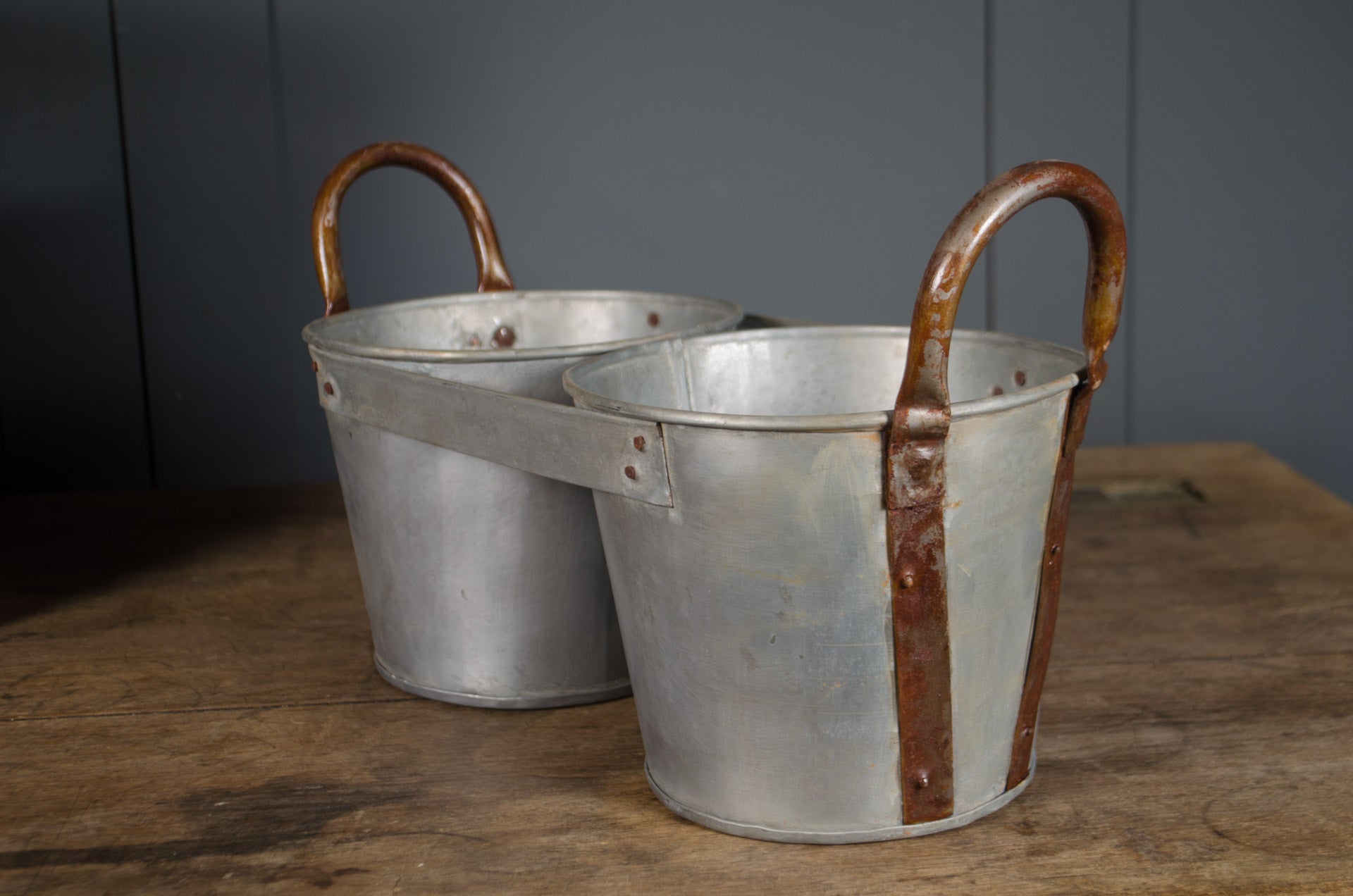 
Millwards Two metal buckets with handles on a wooden surface against a gray wall.