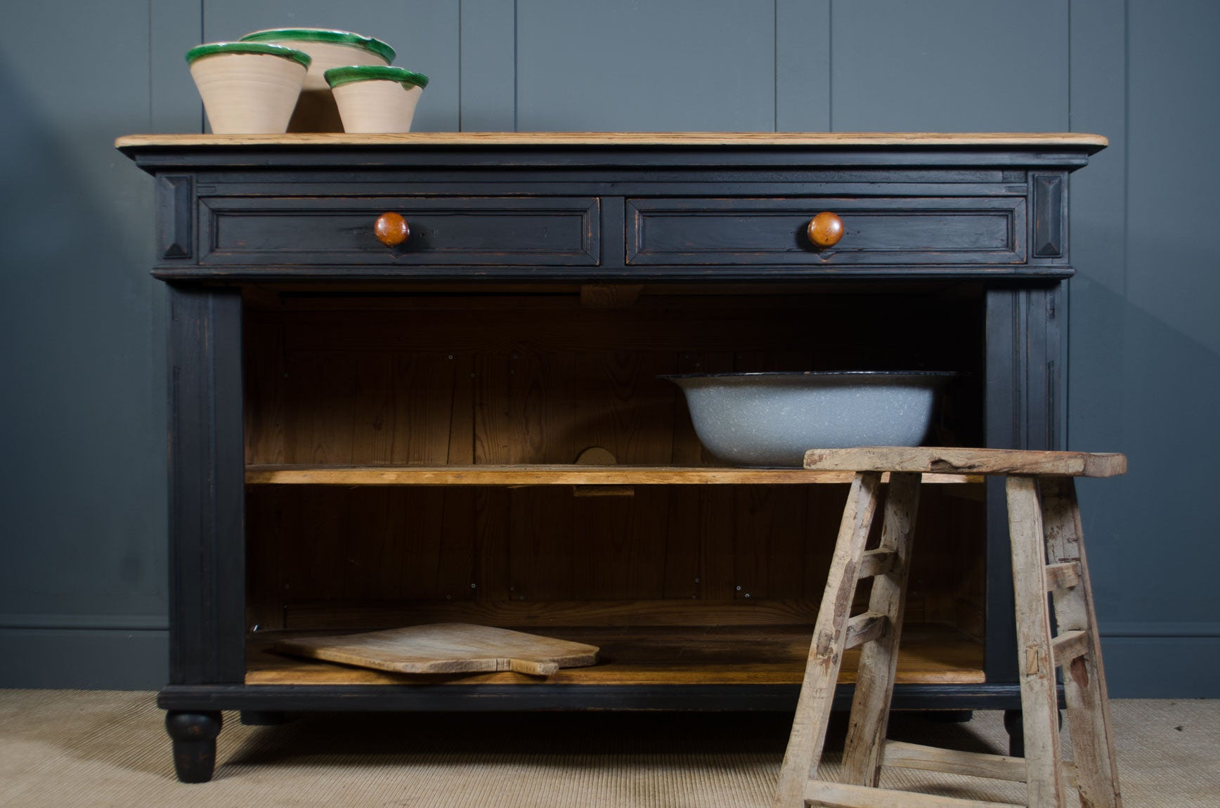 Dark wooden dresser with a white bowl on a wooden stool against a blue wall.