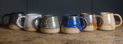 handmade wheel thrown green mugs Row of ceramic mugs in various colors on a wooden surface with a dark background
