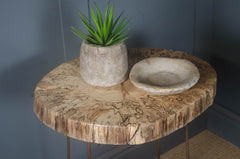 Round wooden side lamp table with a potted plant and a stone bowl against a dark wall.