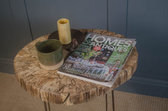 Wooden side table with a mug, candle, and 'Homes & Antiques' magazine against a blue wall.